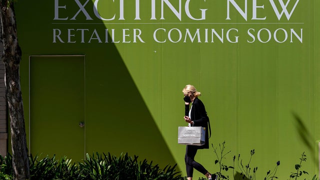 Woman walks by full-frame green sign reading "Exciting new retailer coming soon" 