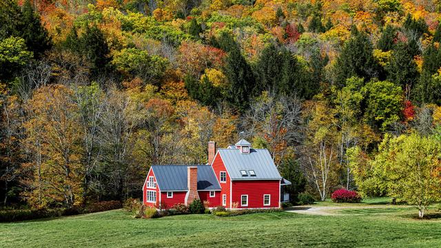 Charming red house flanked by autumn foliage in Vermont. 
