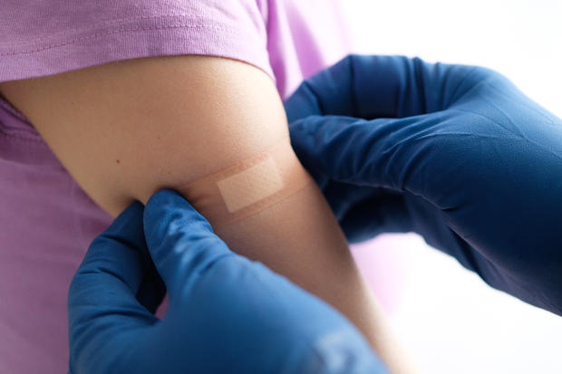 covid vaccine A gloved doctor or health care professional applies a patch or adhesive bandage to a girl or young woman after vaccination or drug injection. The concept of medicine and health care, vaccination and treatment of diseases. First aid services. 