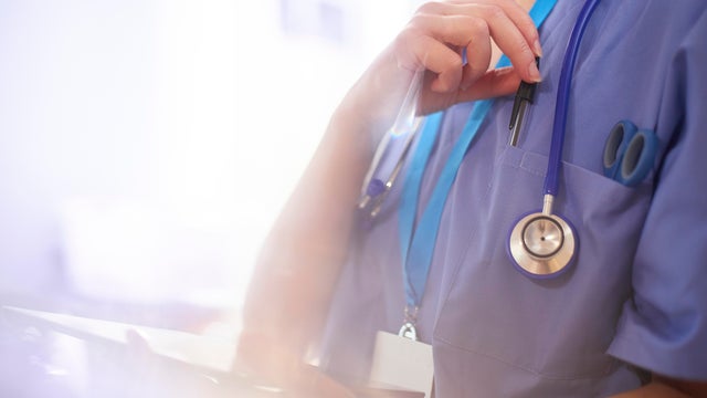 Surgeon using digital tablet in hospital and reaching for her pen 