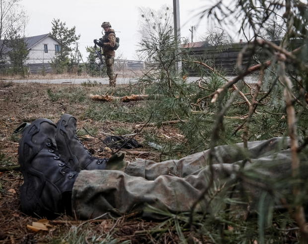 A Ukrainian service member stands near a body of a Russian soldier on the front line near Kyiv 
