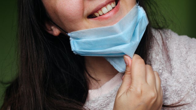 Concept of Covid-19 quarantine or lockdown end. Close up of happy woman taking off her face mask. 