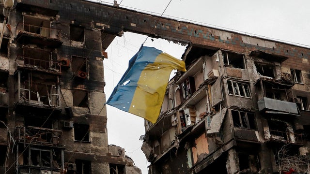 A tattered flag of Ukraine hangs from a destroyed apartment building in Mariupol 
