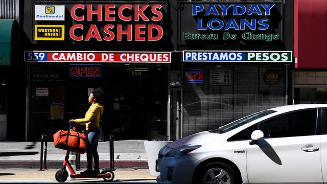 Person rides scooter past "Checks cashed" storefront 