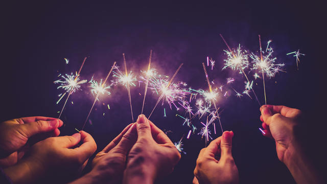Cropped Hands Of People Holding Sparklers At Night 