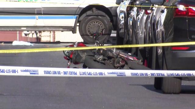 A scooter lays in the road behind police tape. 