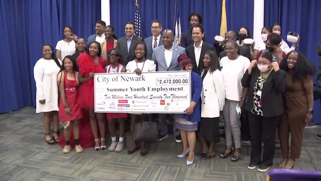 A group of teens, young adults and city leaders stand together. Several people in the front are holding a large check for the city of Newark's summer youth employment program for $2,472,000.00. 