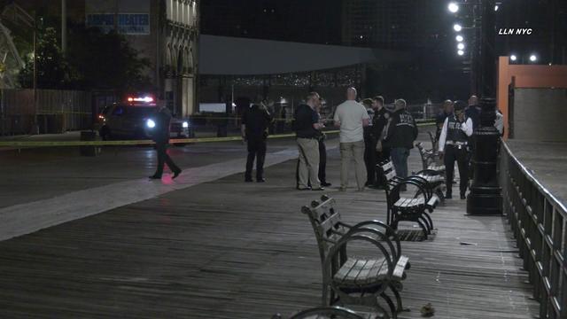 Several police officers and other people stand near crime scene tape on the Coney Island boardwalk. 