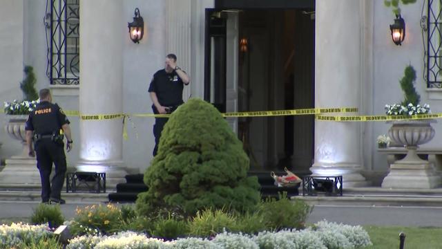 Crime scene tape blocks off the entrance to the Mansion at Glen Cove while two police officers stand outside. 
