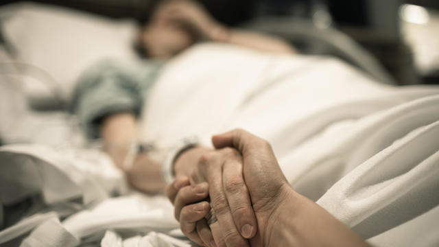 Sick woman lying in hospital bed with hand being held by love one. 
