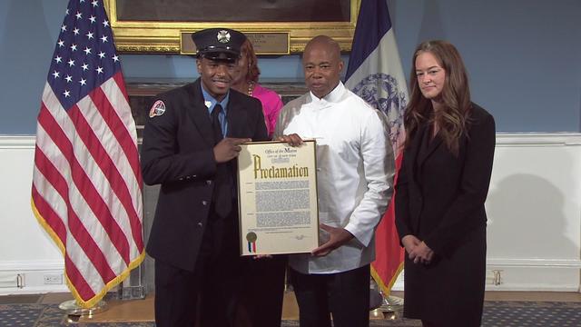 Firefighter Stefon Douglas stands with Mayor Eric Adams, both holding a proclamation 