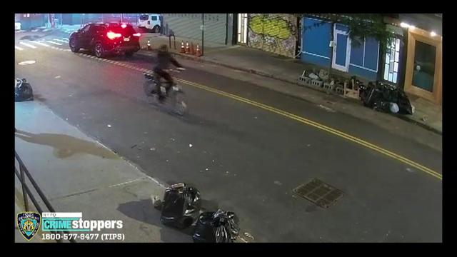 A man in all black rides a bicycle down a street. 