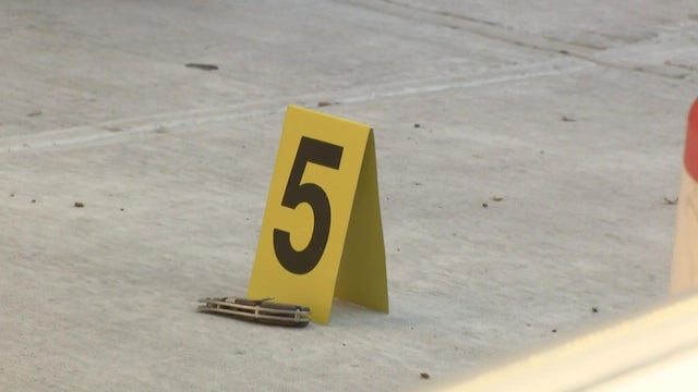 A yellow evidence marked with the number 5 on it sits on a sidewalk next to a pocket knife. 