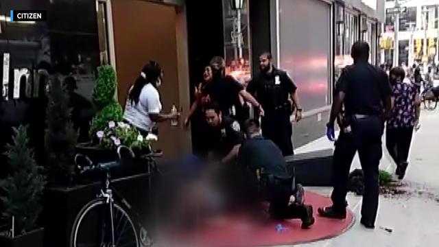A screenshot from a video shows police officers kneeling on the ground next to someone outside a hotel. 
