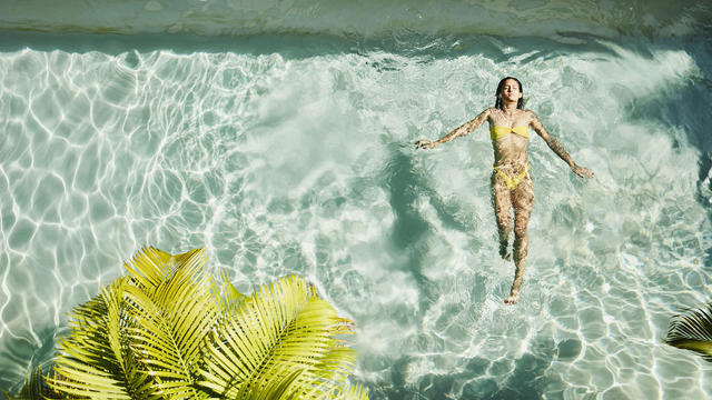 Overhead view of woman floating on her back in pool at outdoor spa 