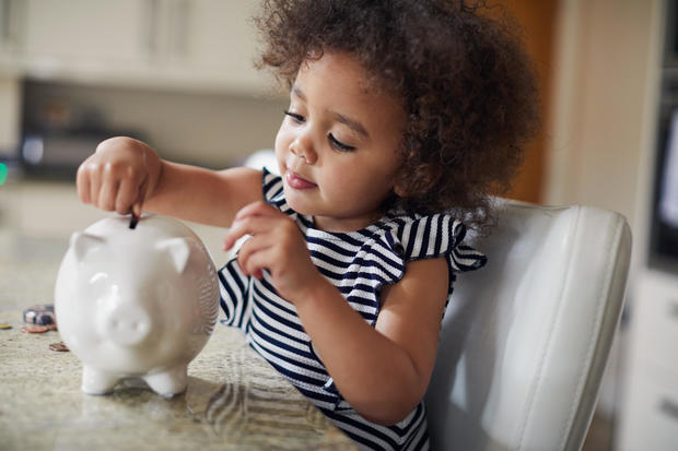 Child saving coins into a piggy bank 