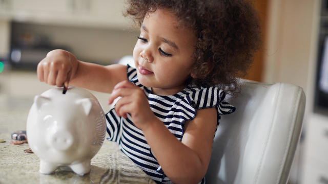 Child putting coins into a piggy bank 