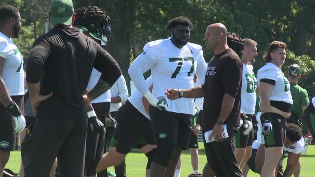 New York Jets head coach Robert Saleh stands on a practice field, speaking to several players. 