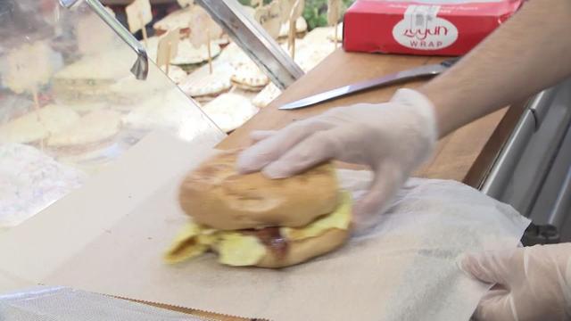 A deli worker prepares a bacon, egg and cheese. 