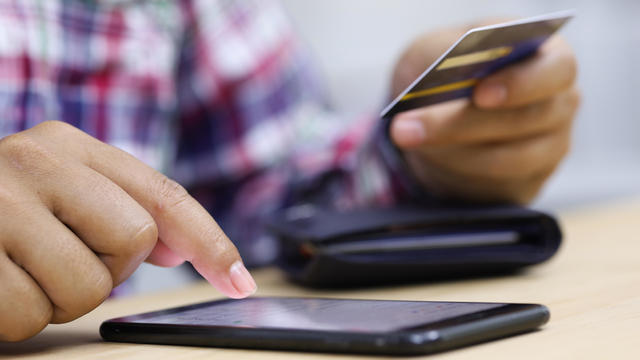 Closeup young man hands holding credit card and using cell, smart phone for online shopping or reporting lost card, fraudulent transaction 