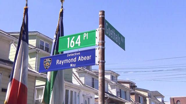 A pole with three street signs -- one reading "Goethals Av," one reading "164 Pl" and one with the NYPD crest reading "Detective Raymond Abear Way." 