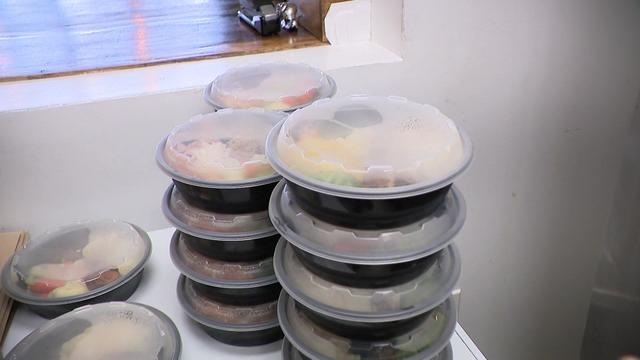 Several stacks of take-out containers filled with food sit on a counter in a restaurant kitchen. 
