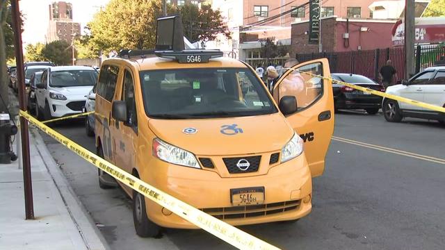 Crime scene tape surrounds a yellow taxi cab parked on a street. 