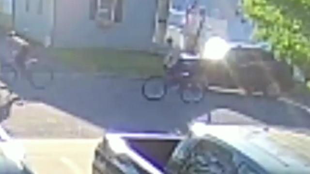 Surveillance video shows two men riding bicycles down a street. 