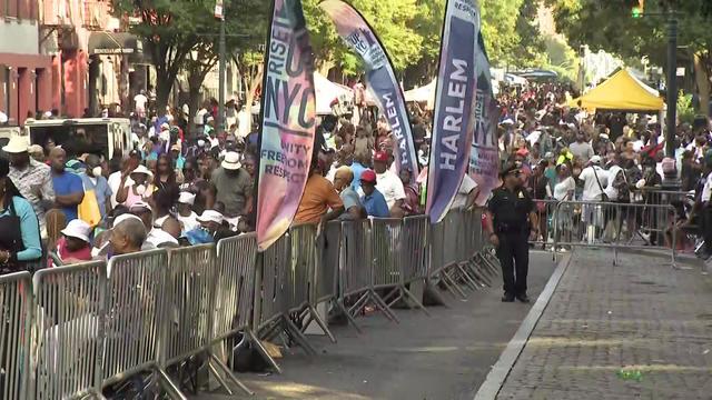 Crowds of New Yorkers stand and sit behind barricades to watch performances. 