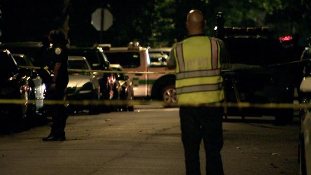 Police officers stand in the street behind crime scene tape. 