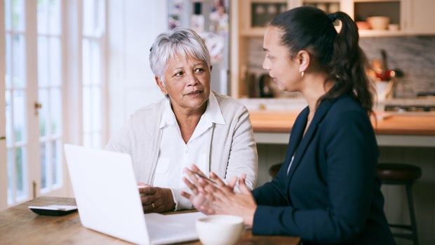 Shot of a senior woman using a laptop during a meeting with a consultant at home 