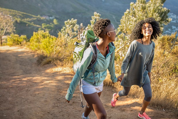 Two happy young women walking hand in hand on a mountain trail outdoors 
