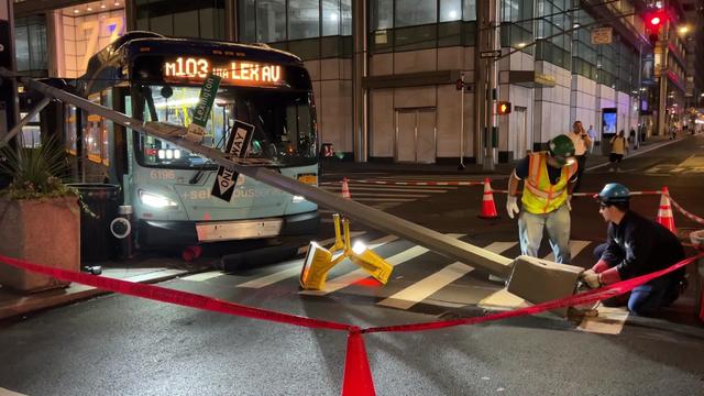 A light pole lays in the street in front of an MTA bus. 