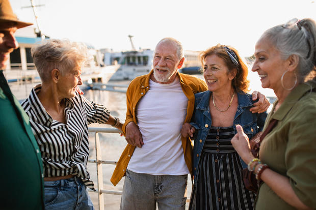 Group of happy senior friends tourists standing in city port, talking. 