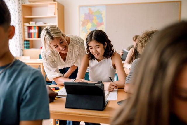 Smiling teacher teaching girl studying on digital tablet in classroom 