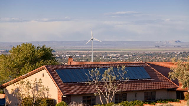 Solar panel on roof of home with wind turbine in background, Housing developments in Palmdale, Los Angeles County, California, USA 