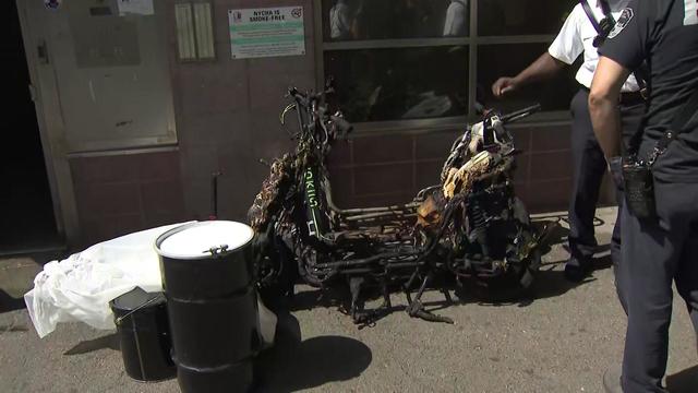 Two severely burned and mangled e-bikes sit outside a building. 