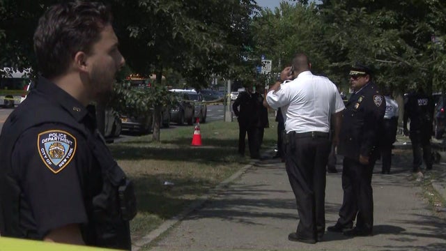 Police stand behind crime scene tape in a park. 