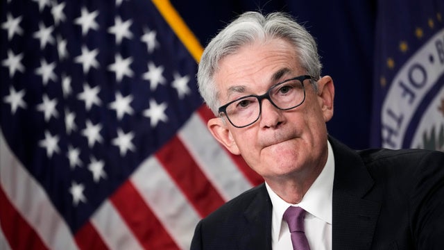 White-haired man with glasses in front of American flag 