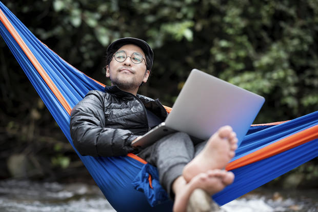 Man lying in hammock using a laptop 