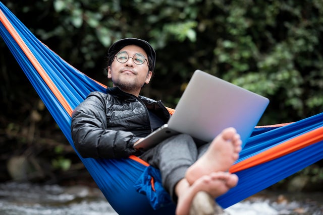 Man lying in hammock using a laptop 