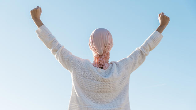 Back view of a woman with cancer raising her arms as a symbol of defeating cancer. 