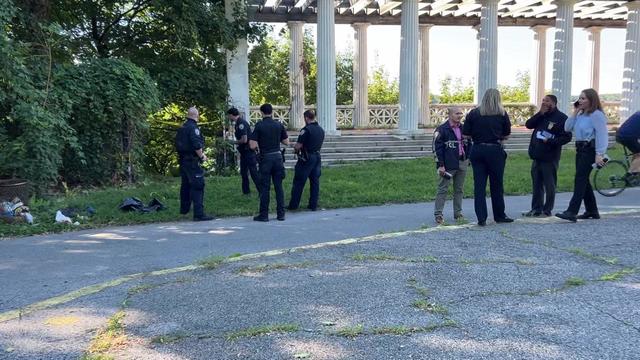 Several police stand on a trail near a raised platform with columns. 