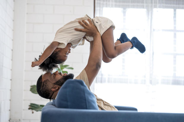 African father lifting daughter in the air face to face.  They are having fun at home on weekends. 