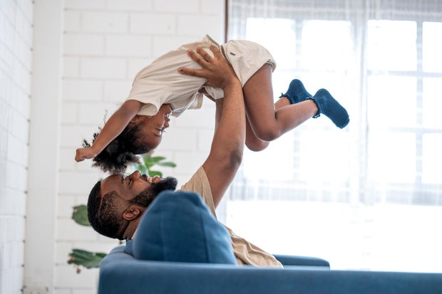 African father picking up daughter in the air, face to face. They are having fun in weekend at home. 