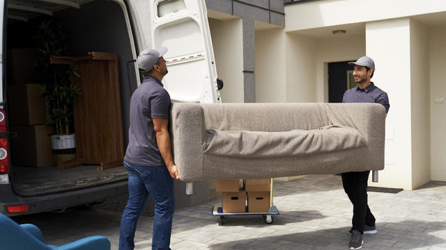 Male delivery coworkers unloading sofa from moving van near house 