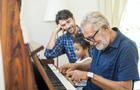 Family spend time happy together. Grandfather playing piano with his granddaughter and son together in living room at home. 
