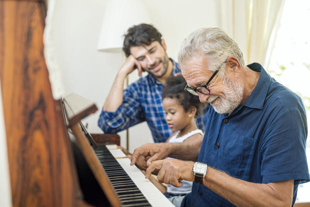 Family spends time together happily.  Grandfather playing the piano together with his granddaughter and son in the living room at home. 