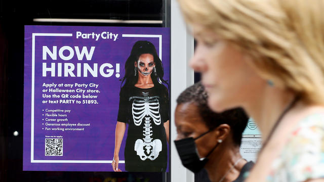 Two women walk by purple "now hiring" sign 