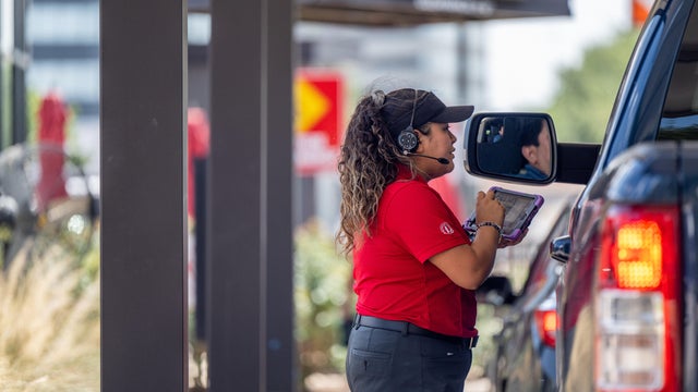 Female worker in red shirt takes an order at a drive-thru 